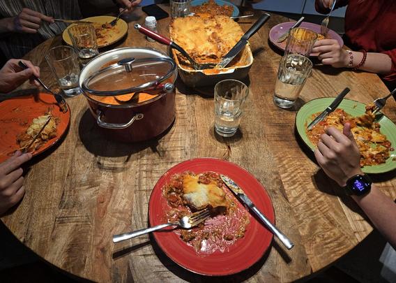 A round dinner table with six plates in the colors of the rainbow with lasagne on them.