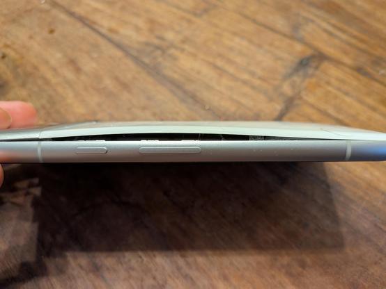Ein weißes Handy mit metallenem Rahmen, von der Seite fotografiert. Es ist so aufgebläht, dass sich ein deutlicher Spalt im Gehäuse gebildet hat.