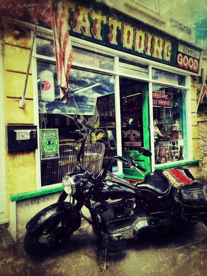 A lowrider motorcycle in front of a tattoo shop. The photo is all grungy and saturated.