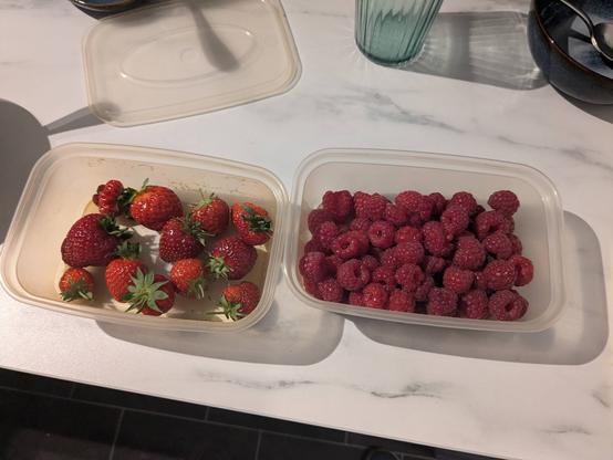 Two plastics tubs of strawberries and raspberries.