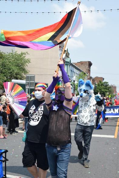 Pup masked marcher holding pride flag aloft in parade.