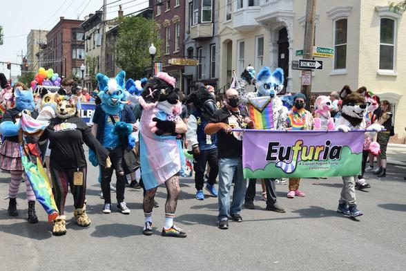Big group of furries turning the street corner behind Eufuria's banner.