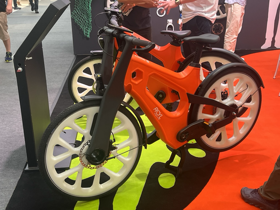 Ein Fahrrad der Marke „RCYL“ („recycle“) mit sehr dickem Rahmen aus rotem Plastik, mit sehr dicken Speichen aus weißem Plastik