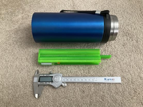 blue metal thermos laying on its side next to a green 3d printed insert and a caliper. the caliper shows relative scale to display the thermos is easily 180mm deep.