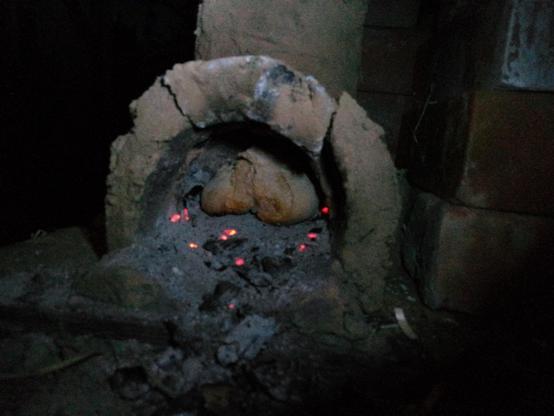 Die halbrunde Ofenöffnung lässt den Blick ins Innere gleiten. Dort befindet sich ein gut gebackenes Brötchen zwischen glühenden Holzstückchen. Mit Taschenlampe aufgenommen, rings herum ist es dunkel.