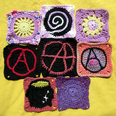8 granny squares lying next to each other on a yellow surface. There are 3 anarchy symbols among them, a cauldron, and a spiral. The others are one colour or vaguely reminiscent of a flower or sun.