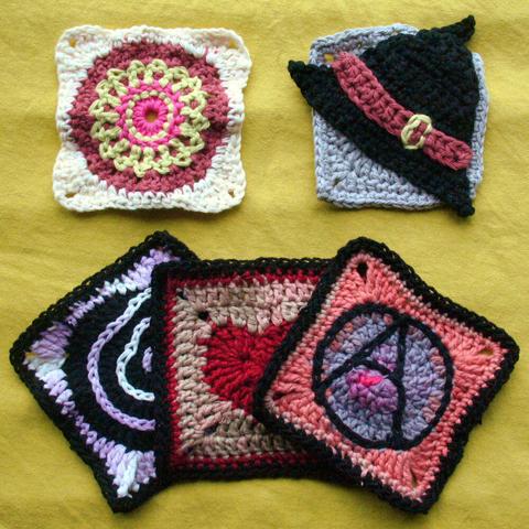 5 granny squares lying next to and over each other on a yellow surface including a witch hat, an anarchy symbol, a heart, and a spiral.