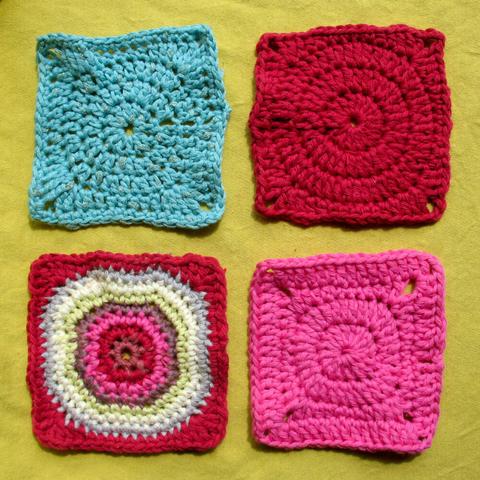 4 blue, red, and yellow granny squares lying next to each other on a yellow surface.