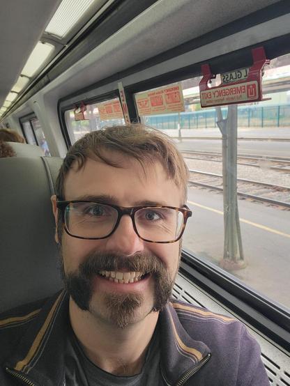 A selfie inside the train. Train tracks and posts are outside the windows behind me.