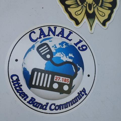 autocollant rond.en son centre la planète terre vue au dessus du continent africain avec un émetteur/récepteur stylisé par dessus et le 27.185 affiché. sur le haut de l'autocollant est inscrit "canal 19” et dessous "citizen band community"