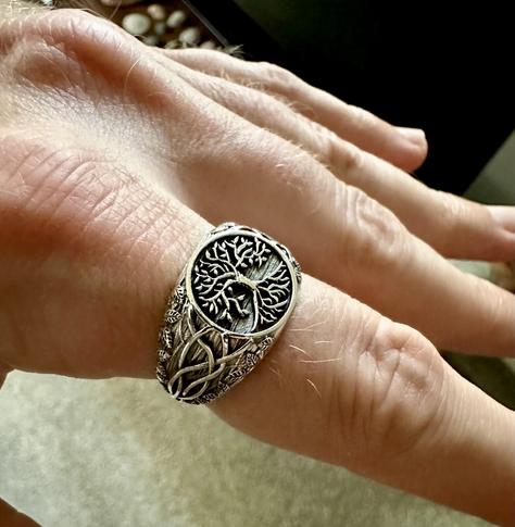 A silver ring on a finger with yggdrasil on it