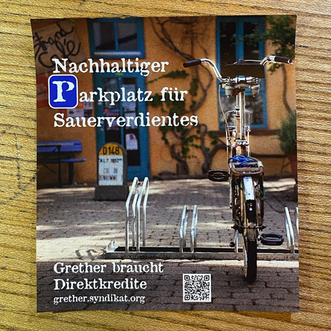 Ein Fahrrad in frühlingshaftem Morgenlicht steht im Innenhof des Grether Geländes - im Hintergrund ist das Strandcafe zu sehen. 
Der Text lautet : Nachhaltiger Parkplatz für Sauerverdientes. Grether brauch Direktkredite.