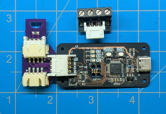 The same printed circuit board, but with parts soldered onto it, and with three other boards in the frame. One board has three connectors , in a "T" configuration, and it is plugged into the main board, splitting the connector into two. A small board with a single resistor is plugged into one side of the splitter board (this is a terminator board). Another board with a large terminal block is next to them.