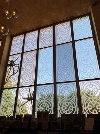 A multipanel etched glass art deco window. I had thought, taking the photo in the space, that there was some sort of decoration applied to two of the panels, but zooming in, I can see that it's unfortunately damage that has been dealt with via temporary tape. No idea what happened. Trees are visible through the glass.
