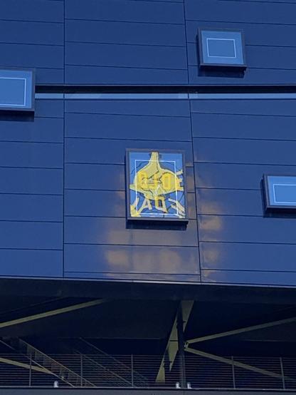 A blue theater facade with three small square windows visible and one larger rectangular window. The larger one reflects a blurry sign from the top of a facing grain elevator. The yellow sig that’s featured is blurry in reflect but says Gold Medal Flour atop the elevator.