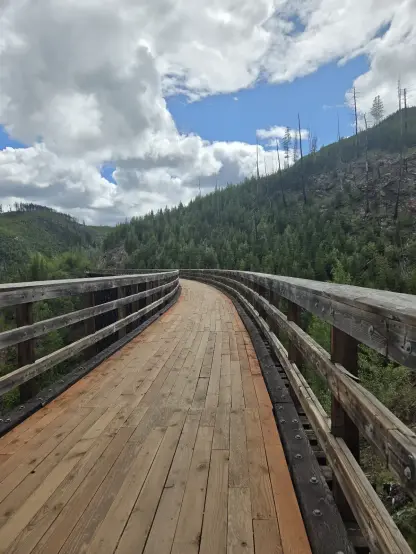 Curved trestle deck, with railing on both sides.  Mountains visible in the background, along with a mixed overcast and partly-sunny sky.