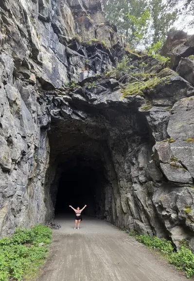Tunnel carved directly into the mountainside.  A woman is standing at the mouth of the tunnel to give some perspective on the size.  Tunnel is many times the height of the woman, since these tunnels were used by trains in the early 1900s.