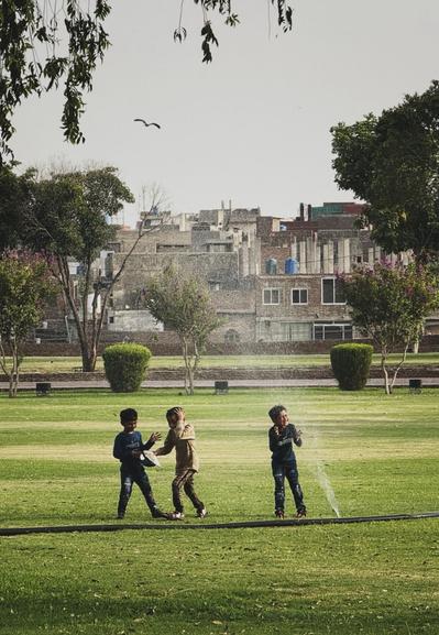 Three kids having a blast with water spraying out of a hose on a hot day in the park