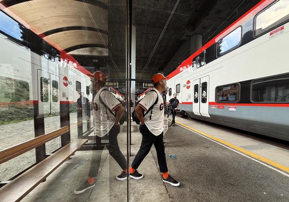 A man in a giants jersey leaves a sheltered bench as the Ctrain pulls into a station. His image is reflected in the shelter window.