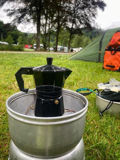 Die schwarze Kaffeekanne auf dem Gaskocher, im Hintergrund Zelt und Radtasche.