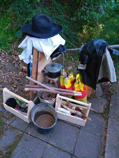Zurechtgestelltes Equipment: 1 Eimer mit Lehm, 2 Werkzeugkisten, Holzstäbe, zwei Sack Holzkohle, 1 Hocker, 1Topf, Blasebalg, Klamotten mit breitkrempigem Hut.