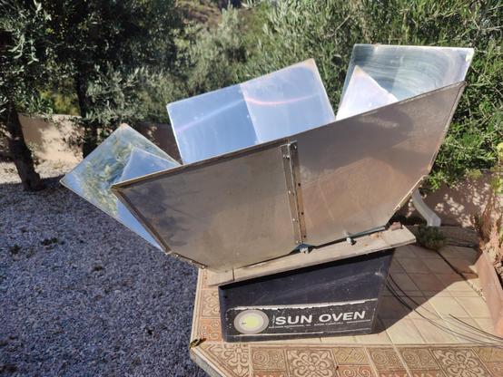 A sun oven with an aluminum parabolic shield directs the suns rays into a cooker