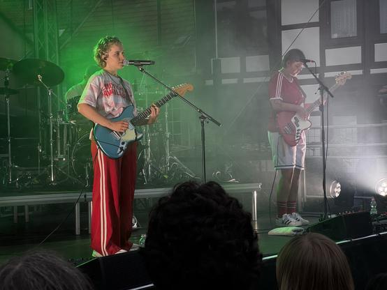 Eva Sauter mit Gitarre am Mikrofon und ihre Bassistin auf der Bühne vor grünem Licht. Ok.Danke.Tschüss rockt gut gelaunt den Abend