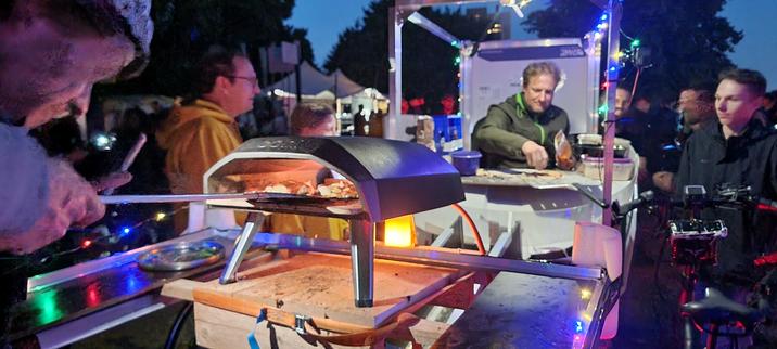 Zwei Pizzabäcker bereiten auf einem Lastenrad und auf einem Anhänger Pizza zu.