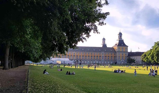 Schloss Bonn mit Hofgarten in der Abendsonne und Menschen auf der Wiese.