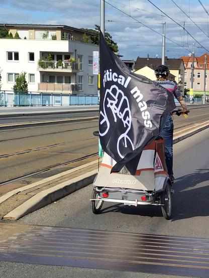 Fahrrad und Anhänger mit großer schwarzer Fahne mit dem Critical-Mass-Logo.