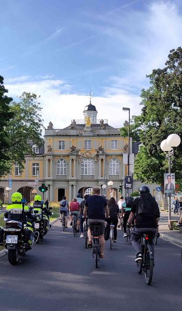 Radfahrende mit Polizeibegleitung auf Motorrad kurz vor der Durchfahrt durch das Koblenzer Tor in Bonn.