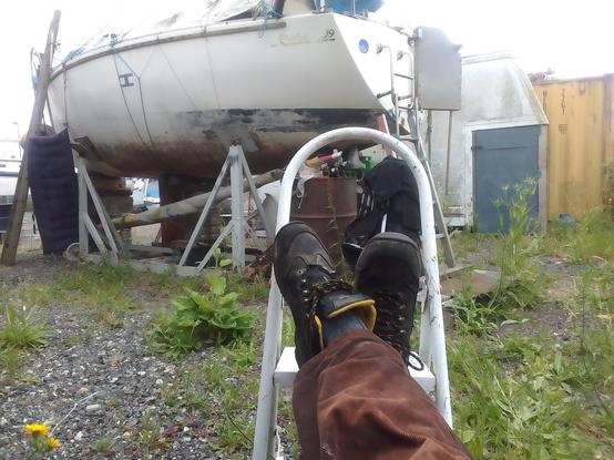 View with feet up, hidden away behind a small yacht high and dry in a steel cradle in a boatyard
