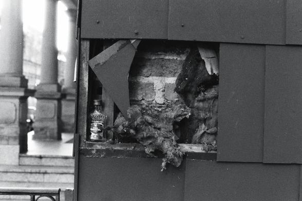 A bw photo of a hole in a wall filled with a small vodgar bottle
