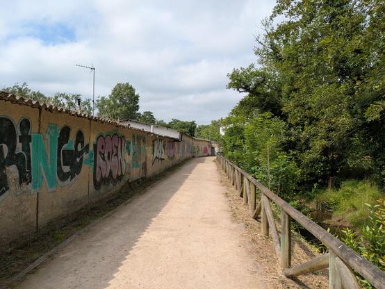 Paisaje de un camino de tierra junto a un riachuelo con unas casas con pintadas a la izquierda