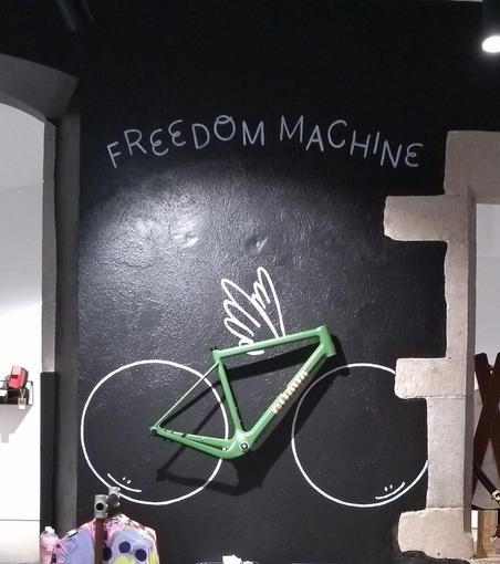 Ein Blick in den Guava-Laden in Girona. Als Dekoration ein grüner MTB-Rahmen auf anthrazitfarbener Wand, die Reifen sind stilisiert in weiß aufgemalt, ebenso wie ein kleines Flügelpaar am Oberrohr.
Darüber in unregelmäßiger Blochschrift "FREEDOM MACHINE".