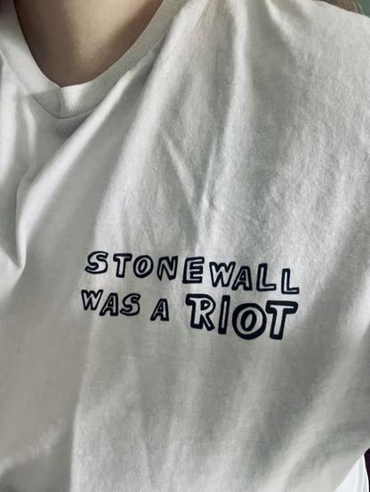 A close-up of a white t-shirt displaying the text "STONEWALL WAS A RIOT."