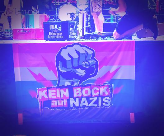 Ausschnitt einer Konzertbühne auf dem Eschweger Johannisfest. Auf der Bühne steht ein Kasten Eschweger Bier, vom Bühnenrand hängt eine Fahne 'Kein Bock auf Nazis'. Das Ganze ist stark vignettiert und ins Blaue verfremdet