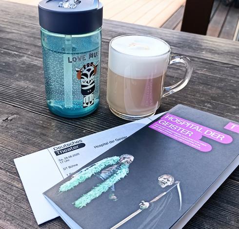 Ticket Programmheft ein Becher Milchkaffee und eine Trinkflasche mit Wasser, auf dem ein Zebra mit Kopfhörern und der Text LOVE MUSIC zu sehen sind