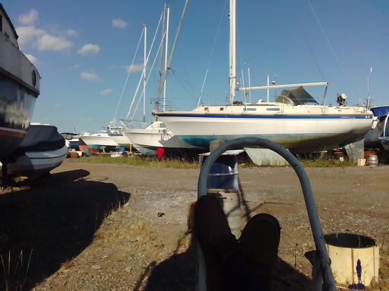 View feet up in the shade under the bow. Various shadows cast across ground and on the hulls of boats
