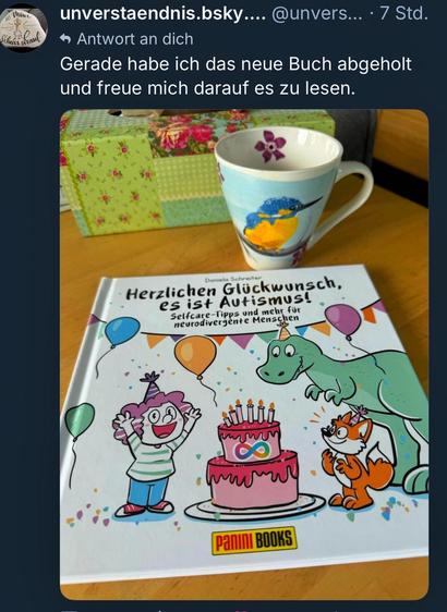 Foto: auf einem Tisch liegt mein neues Buch „herzlichen Glückwunsch, es ist Autismus!“, daneben steht eine Tasse mit einem Eisvogel-Motiv