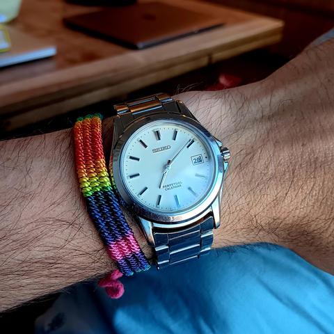 Seiko SBQK079 [JDM] Perpetual Calender with an off white dial and baton indices, with minimal lime. It also has a date complication. Steel case with a steel strap. On the same wrist is a rainbow band.