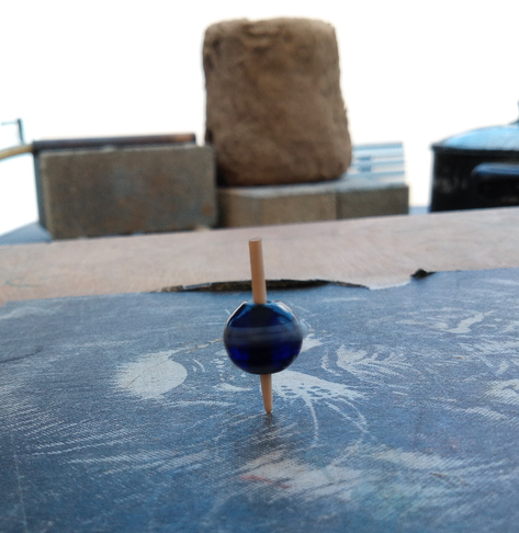 Ein Glasperlenkreisel dreht sich schnell, er steht auf der Spitze. Im Hintergrund sieht man etwas unscharf den Ofen.