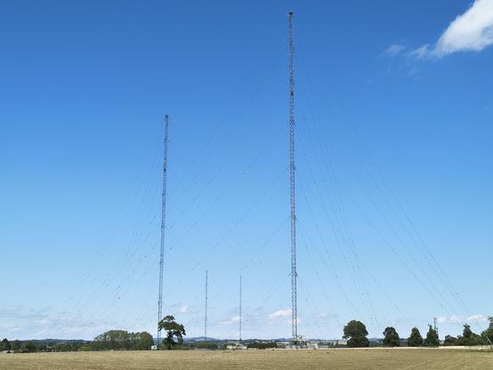 Leerer Acker, im Hintergrund zwei sehr hohe Antennenmaste vor blauem Himmel.
