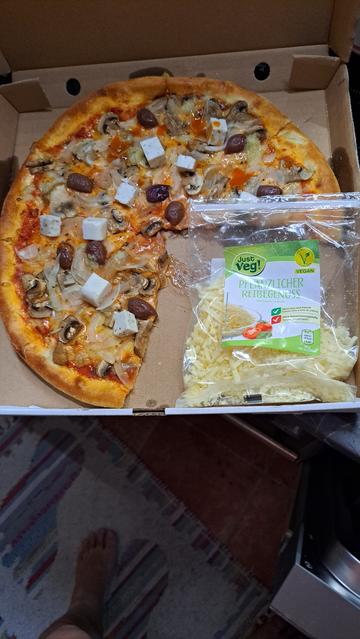 Eine Pizza in einem Pizzakarton und ein Päckchen Veganer Schmelzkäse daneben