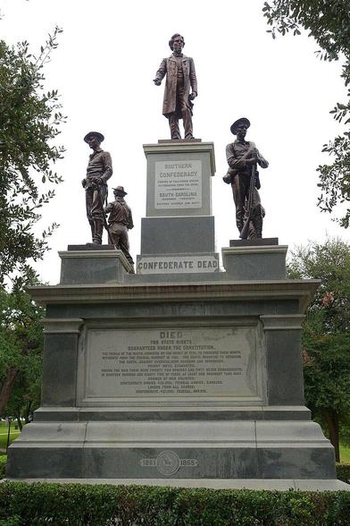 The image depicts a monument dedicated to the Confederate Dead. The monument is composed of a large stone base with inscriptions and five bronze statues, four of which are visible . The central statue is of Confederate States President Jefferson Davis in a long coat, standing on a pedestal with a plaque that reads "SOUTHERN CONFEDERACY" and "SOUTH CAROLINA DECEMBER TWENTIETH EIGHTEEN HUNDRED AND SIXTY." Flanking the central figure  three soldiers can be seen. The base of the monument has a plaque that reads "CONFEDERATE DEAD" and includes a detailed  and historically misleading inscription about the Confederate soldiers' fight for slavery and the number of engagements and casualties. The dates "1861" and "1865" are inscribed at the bottom, marking the beginning and end of the Civil War. The monument is set in the park-like area of the Texas State Capitol, with trees and greenery in the background.

Text provided by @altbot, edited by @jemmesedi