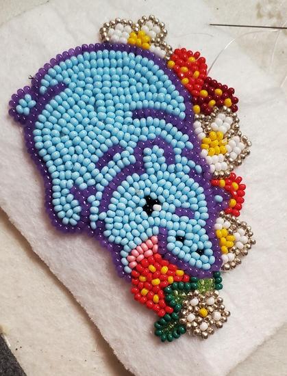 an in progress beaded medallion made by kiamichi of a baby hippo in blue eating a strawberry in a field of strawberries and their flowers.