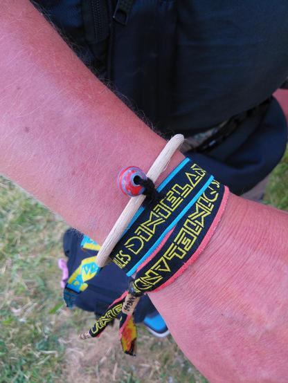 Ein rötlich sonnenverbrannter Unterarm mit einem Rattanreifen am Handgelenk, an dem eine rotblaue Glasperle befestigt ist. Zwei weitere Bänder sind am Arm, jeweils beschriftet mit "Dixieland".