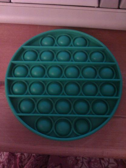 A green, flat, circular popper fidget toy.