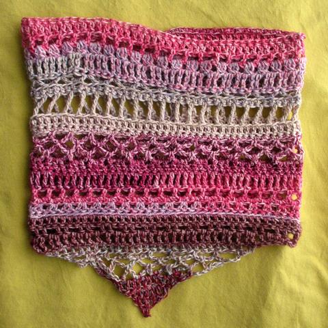 Crochet cowl with different stitches and pink, white, grey, and purple colours, lying flat on a yellow surface.