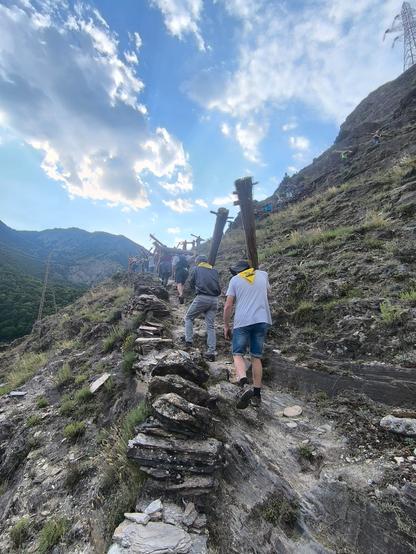 People carrying the wooden trunks (falles) up the mountain in the daylight.